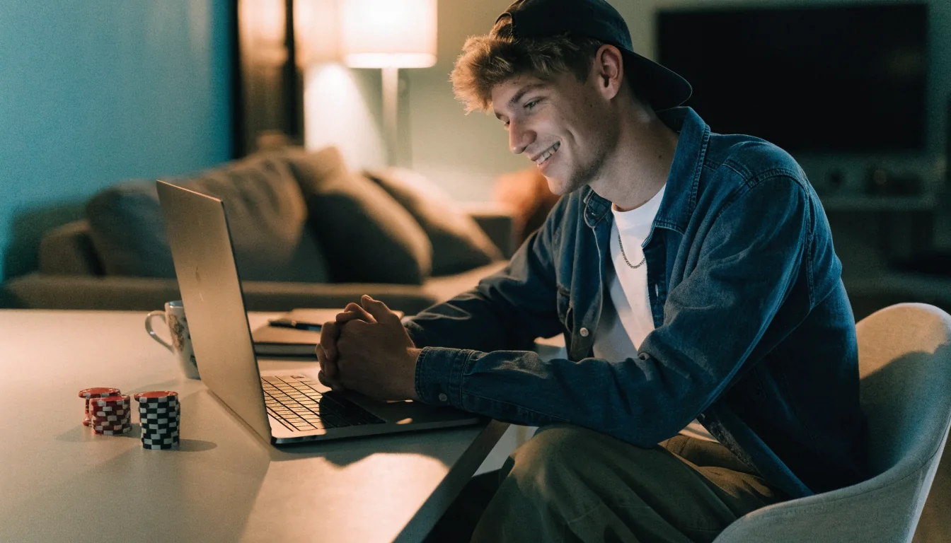Junger Mann zuhause am Laptop mit Pokerchips und Kaffee